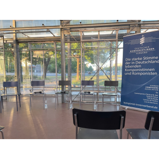 BHROX bauhaus reuse, Glasbau innen, Stühle, Mikrofone, Rollup Banner DKV: "Die starke Stimme der in Deutschland lebenden Komponistinnen und Komponisten"; Berlin; 13.05.2024<br>(Foto: Alexandra Klein)